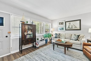 A living room with a white sofa, a wooden cabinet, a coffee table, and a window with blinds.