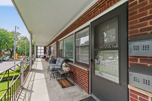 A covered porch with a brick wall, a sliding glass door, and a grill unit.