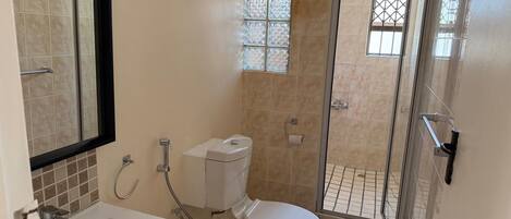 Un baño con bañera, inodoro y zona de ducha con mampara de vidrio.