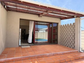 A covered patio with a tiled floor, a sliding glass door, and a metal gate. - Beautiful 3-bedroom house 10 Sleeper - in Cape Town perfect for your getaway (CAPE TOWN)