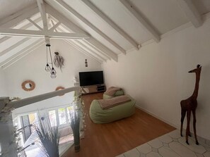 A room with a wooden floor, a green bean bag, a television, and a giraffe statue. - Charming duplex with swimming pool (Saint-François)