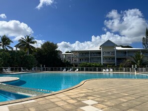A swimming pool with a tiled deck, lounge chairs, and a building with balconies in the background. - Charming duplex with swimming pool (Saint-François)