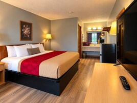 A hotel room with a bed, bedside table, lamp, and a TV.