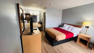 A hotel room with a bed, bedside table, lamp, and a desk with a mirror and lamp.