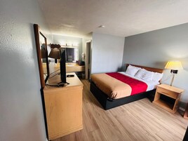 A hotel room with a bed, bedside table, lamp, and a desk with a mirror and lamp.