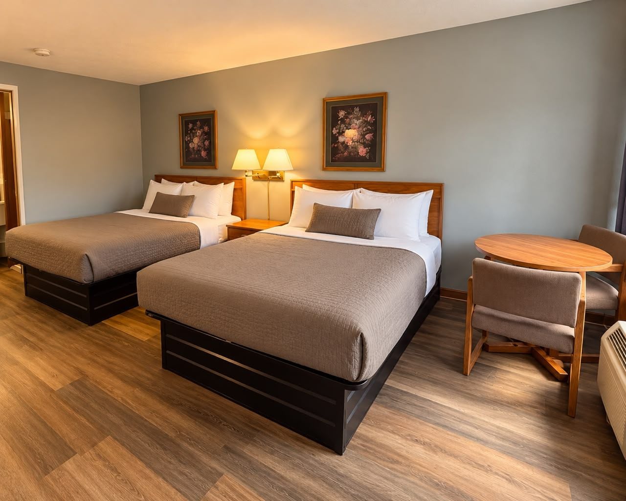 Hotellihuone, jossa on kaksi sänkyä, pieni pöytä ja kaksi tuolia.
