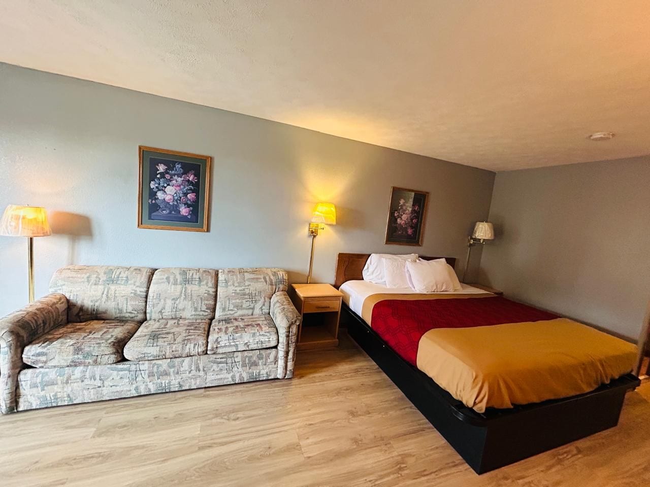 Una habitación con un sofá, una cama, dos mesitas de noche y dos lámparas de pared.