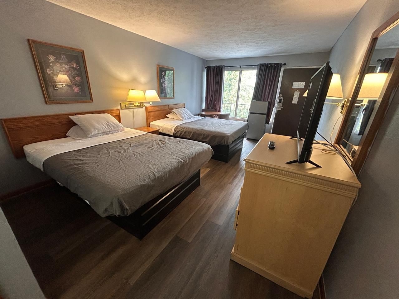 Habitación de hotel con dos camas, un escritorio, un espejo y una ventana con cortinas.