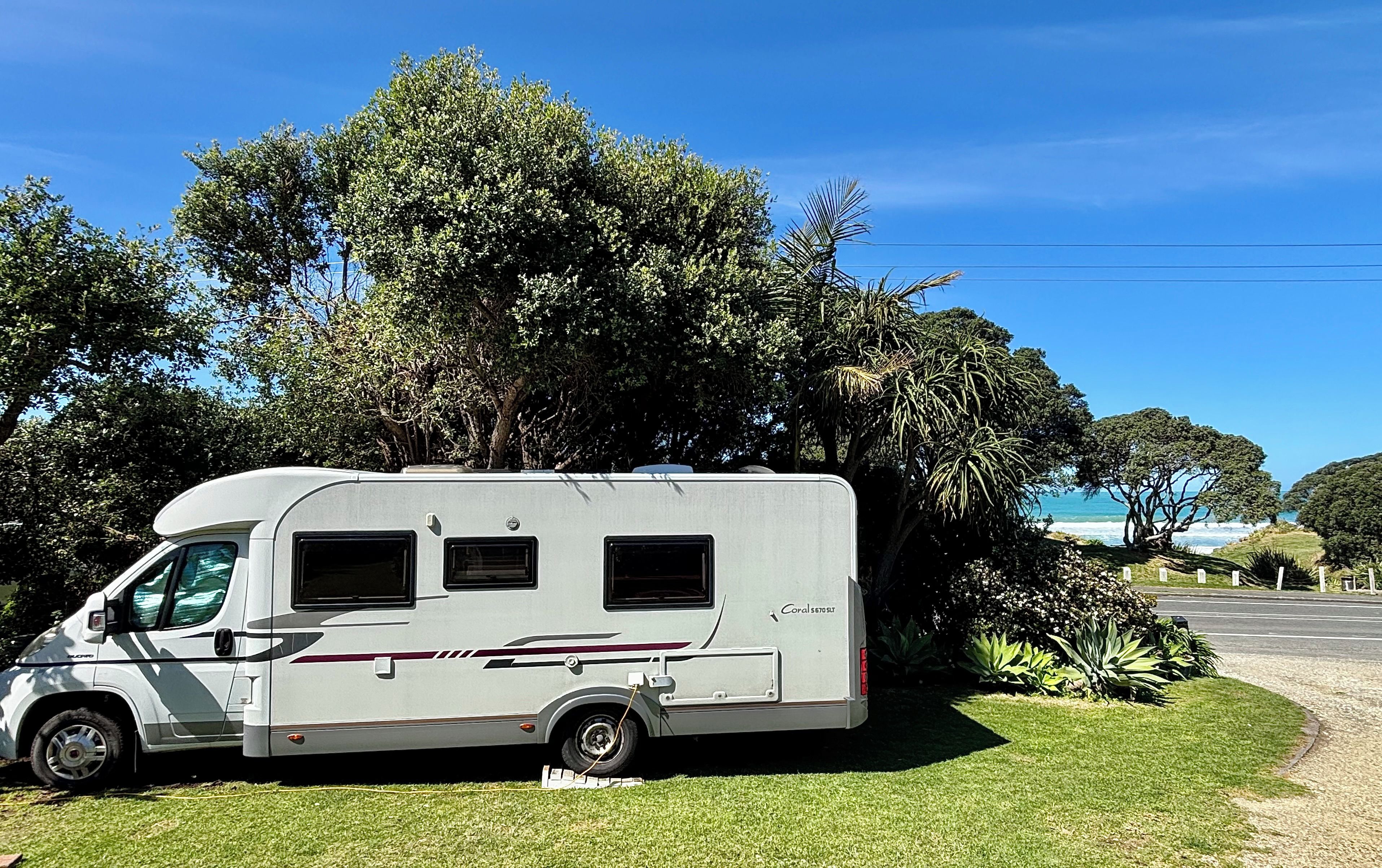 Ein stehender Wohnmobil auf einer Grünfläche mit Bäumen im Hintergrund und blauem Himmel.