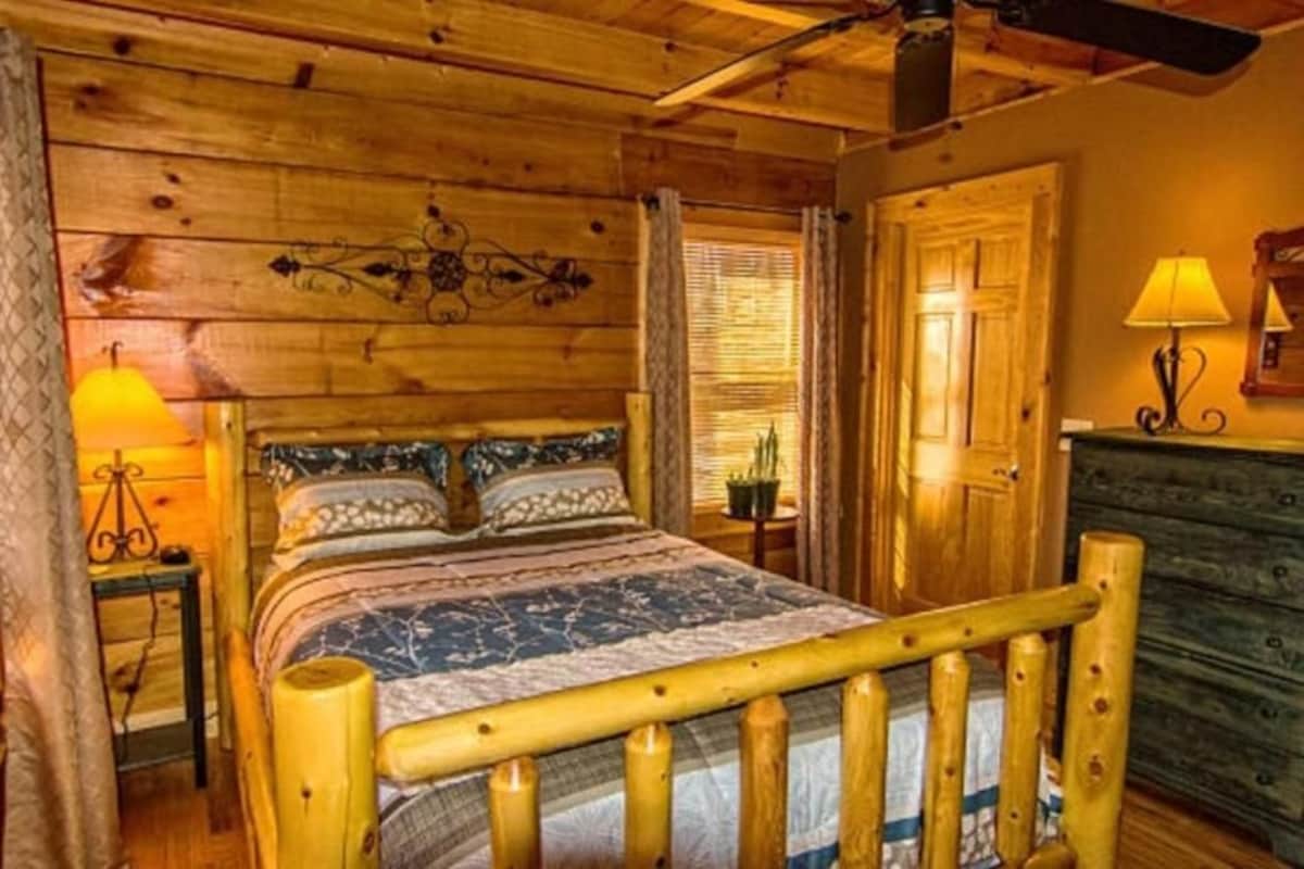 Dormitorio de cabaña de madera con cama, mesita de noche, lámpara y cómoda.