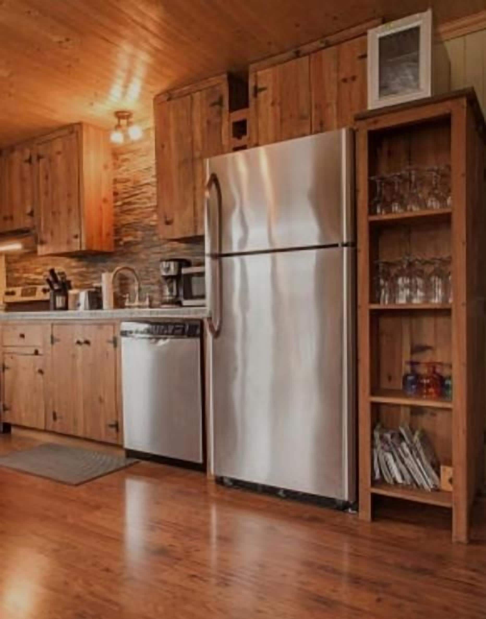 A kitchen with wooden cabinets, a stainless steel refrigerator, and a built-in bookshelf with glassware.