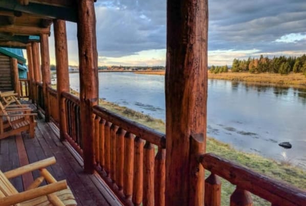 A wooden deck with a railing overlooking a calm body of water, surrounded by trees. - Bush Pilot Hunter s Retreat Lodge (Iliamna)