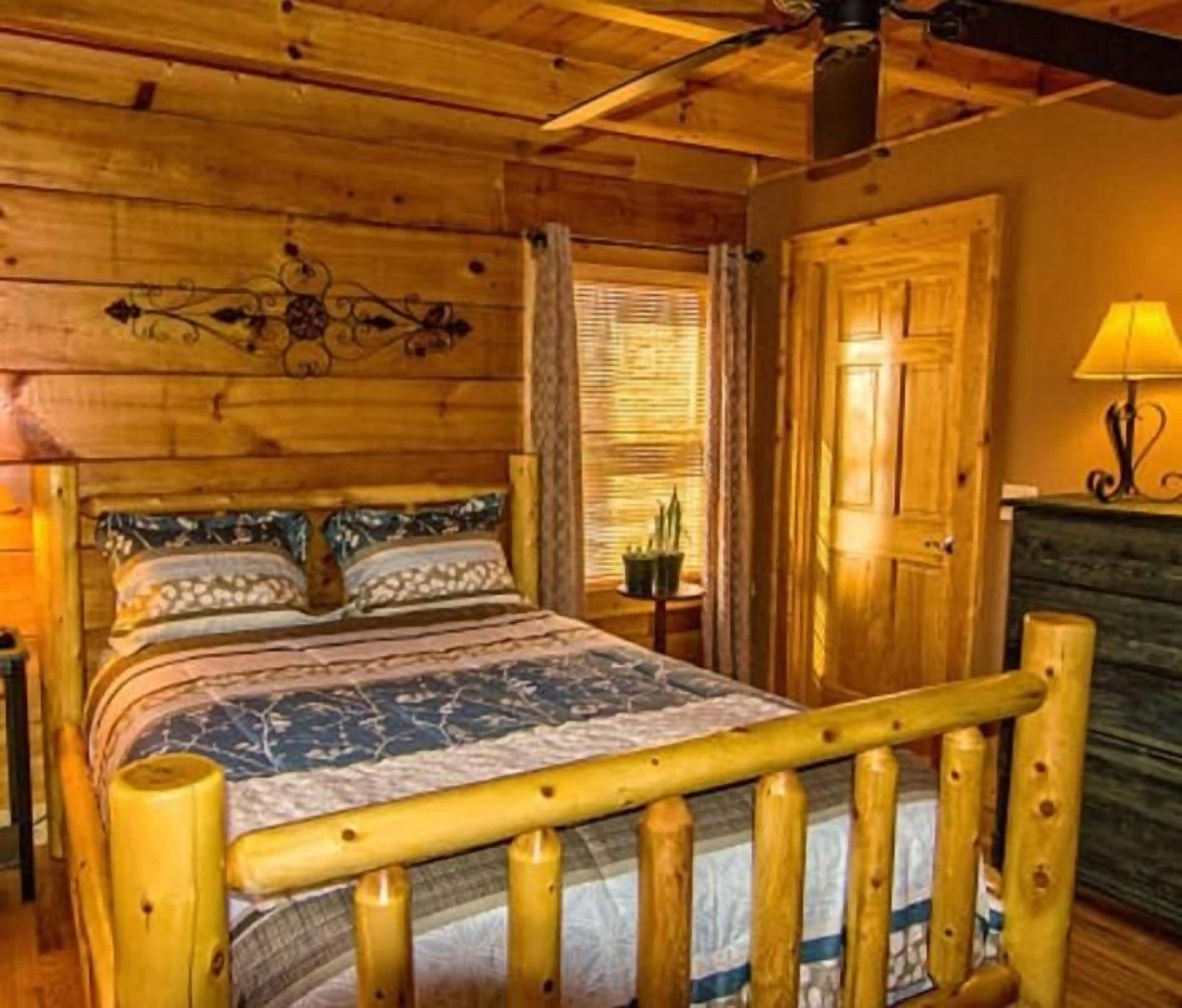A wooden cabin interior with a bed, a nightstand, a lamp, and a door.