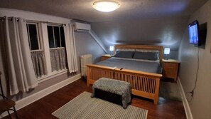 Una camera da letto con un letto in legno, due comodini, un tavolino e una finestra con tende, e una televisione appesa al muro.