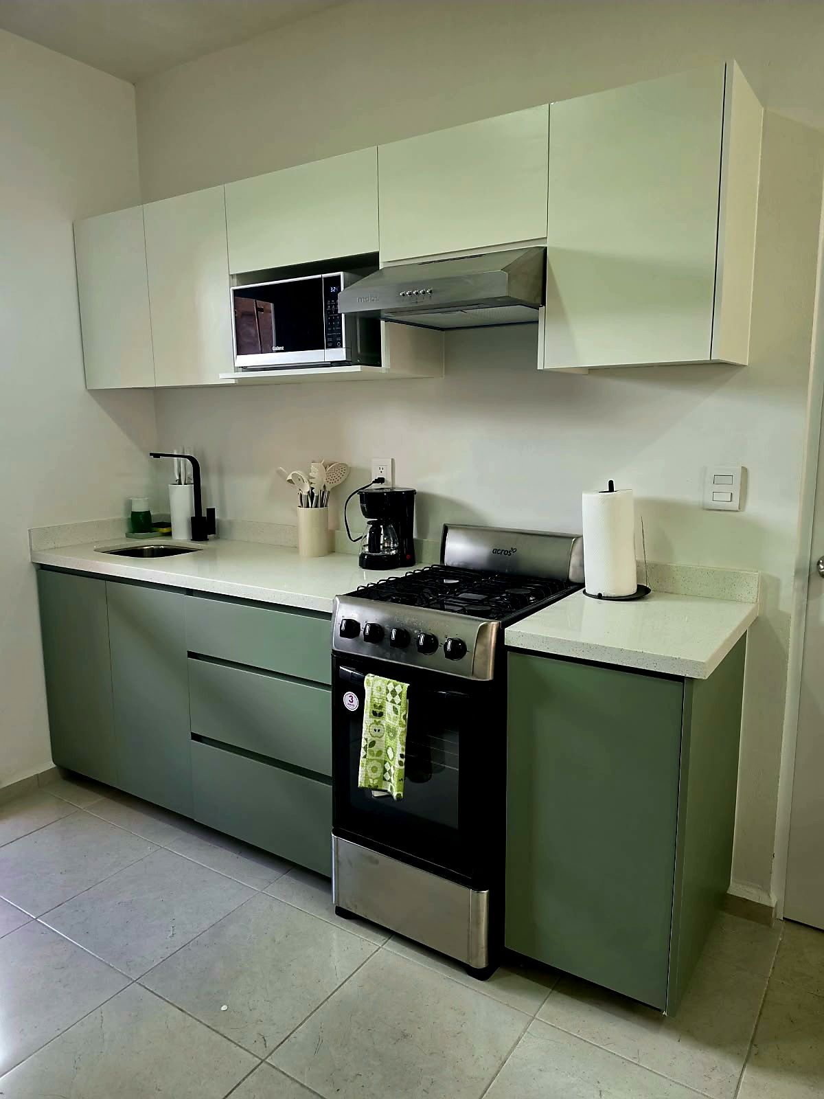 Une cuisine compacte équipée d’une cuisinière à gaz, d’un four à micro-ondes et d’une machine à café.