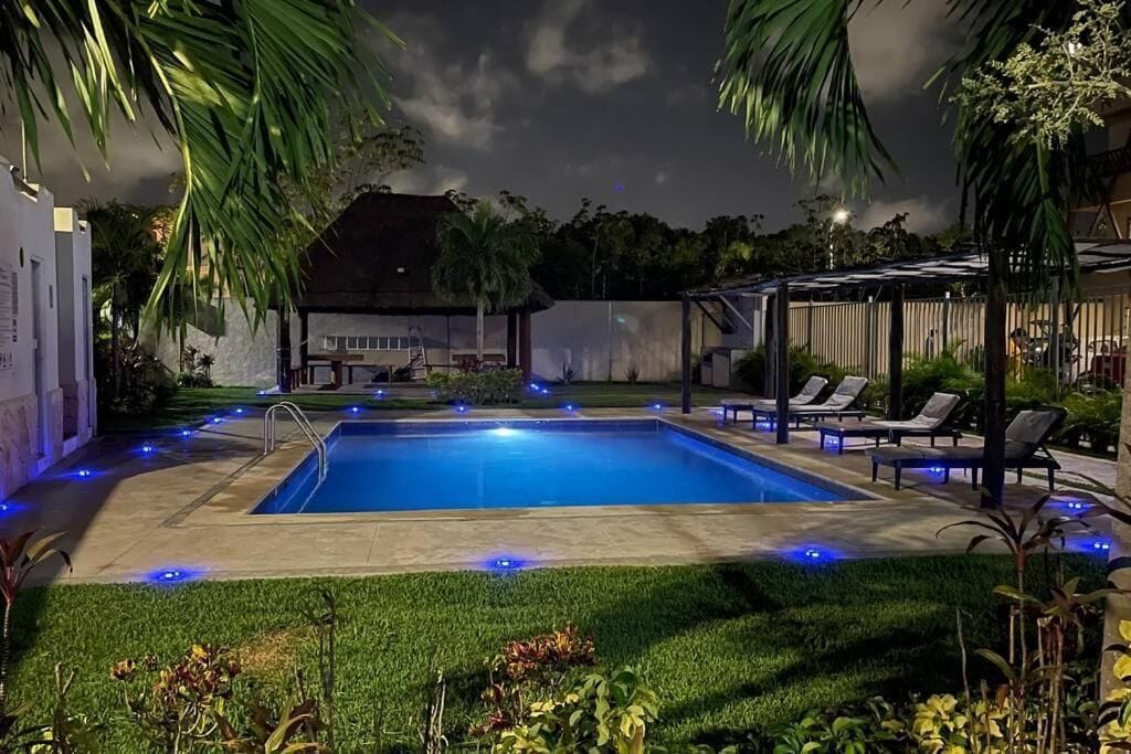 Une piscine rectangulaire entourée d’une terrasse, de chaises longues et d’un espace salon abrité.