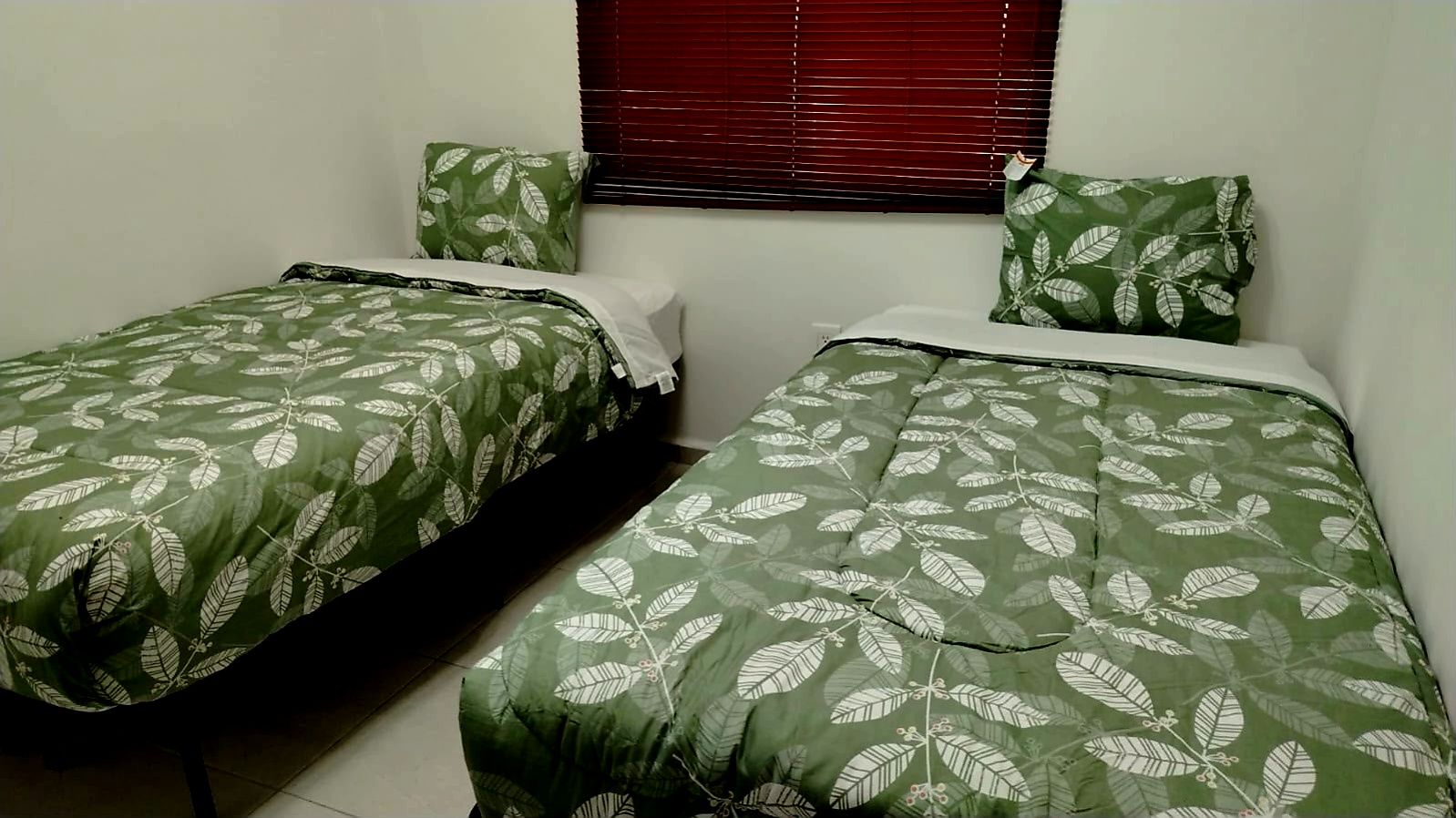 Une chambre avec deux lits simples, chacun recouvert d’une couvre-lit à motifs de feuilles vertes et agrémenté d’oreillers assortis.