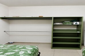 A room with a bed, a green storage unit with shelves, and a radiator.