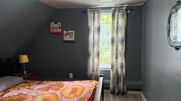 A bedroom with a bed, a nightstand, a lamp, a window with curtains, and two wall art pieces.