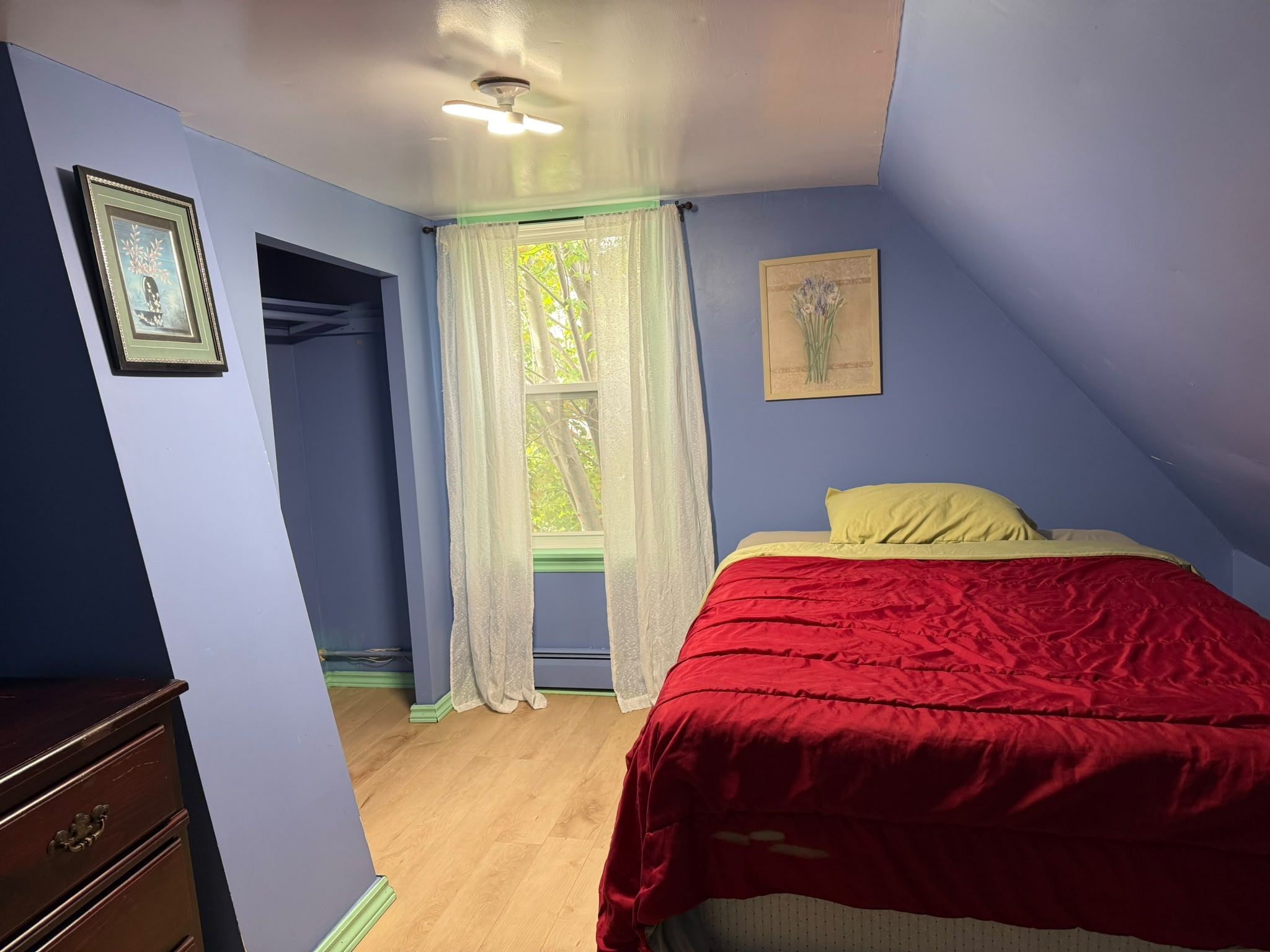 A bedroom with a bed, a window with curtains, a dresser, and a ceiling fan.