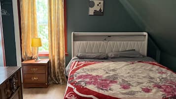 A bedroom with a bed, a nightstand, a lamp, a window with curtains, and a wall-mounted picture.
