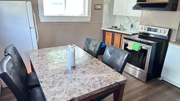 A kitchen with a dining table, chairs, a refrigerator, an oven, and a window.
