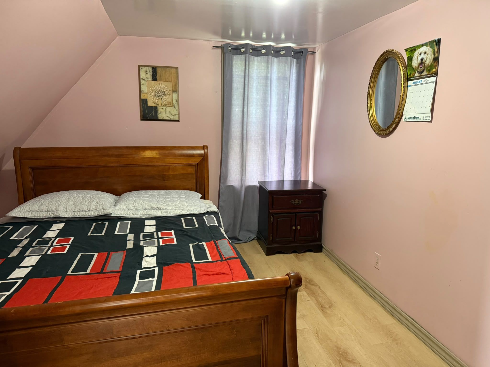A bedroom with a wooden bed, a nightstand, a mirror, and a calendar on the wall.