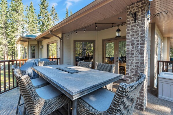 An outdoor patio with a dining table and wicker chairs, surrounded by a stone wall and a wooden deck.