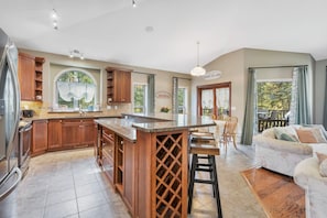 A spacious kitchen with wooden cabinets, a large island, and a dining area with a sofa and chairs. - Chateau country cottage-inspired retreat on 5 majestic, wooded acres. (Mountain View County)