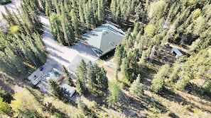 A remote cabin surrounded by dense forest, with a clear driveway leading to the entrance. - Chateau country cottage-inspired retreat on 5 majestic, wooded acres. (Mountain View County)