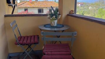 Un balcone con un tavolo, due sedie, una pianta in vaso e vista su edifici e montagne.