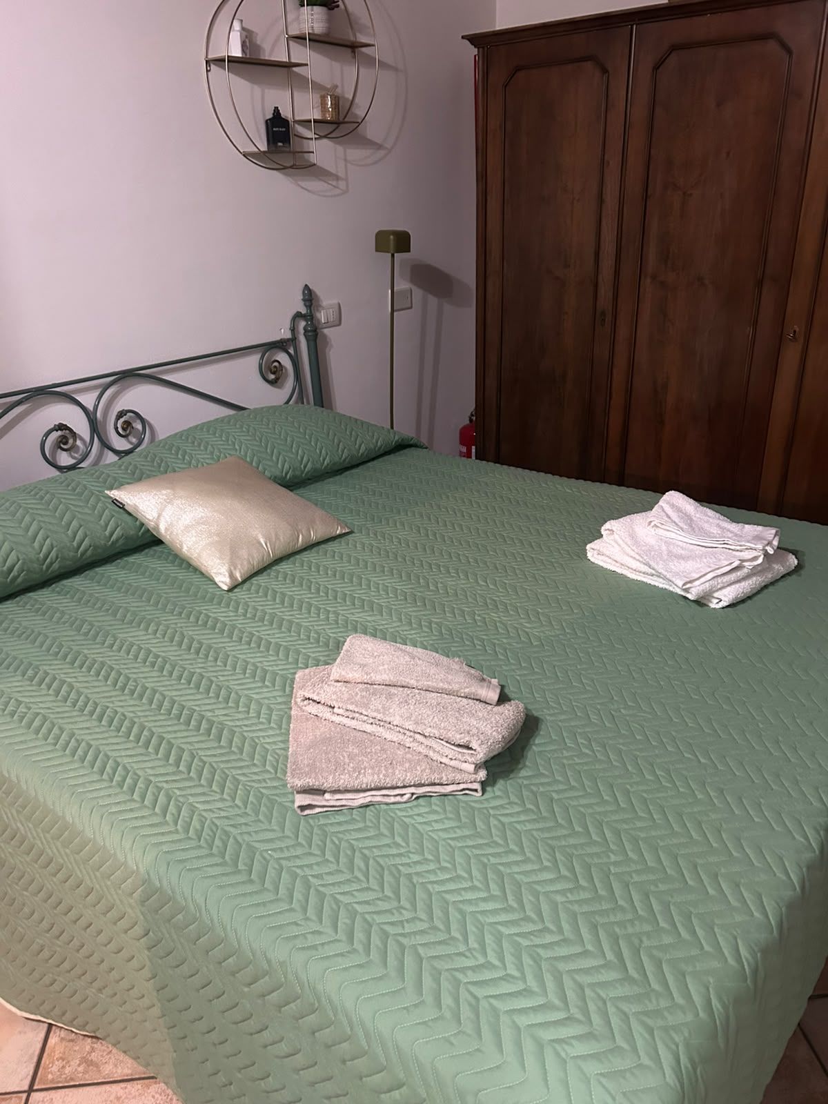 Un letto con una coperta verde, un cuscino e asciugamani piegati.