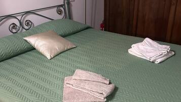 Un letto con una coperta verde, un cuscino e asciugamani piegati.