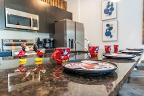 A kitchen counter with Mickey Mouse figurines, a red mug, and a plate with a Mickey Mouse design. - 3BR Townhome | Themed Room + Pool | Gated (Kissimmee)