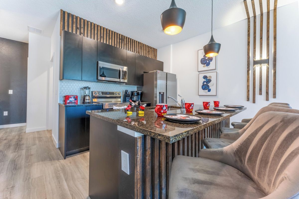 A modern kitchen with dark cabinetry, a central island, and pendant lighting.