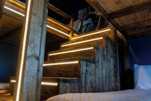 Een houten trap met verlichte treden die leidt naar een bed met een wit kussen.