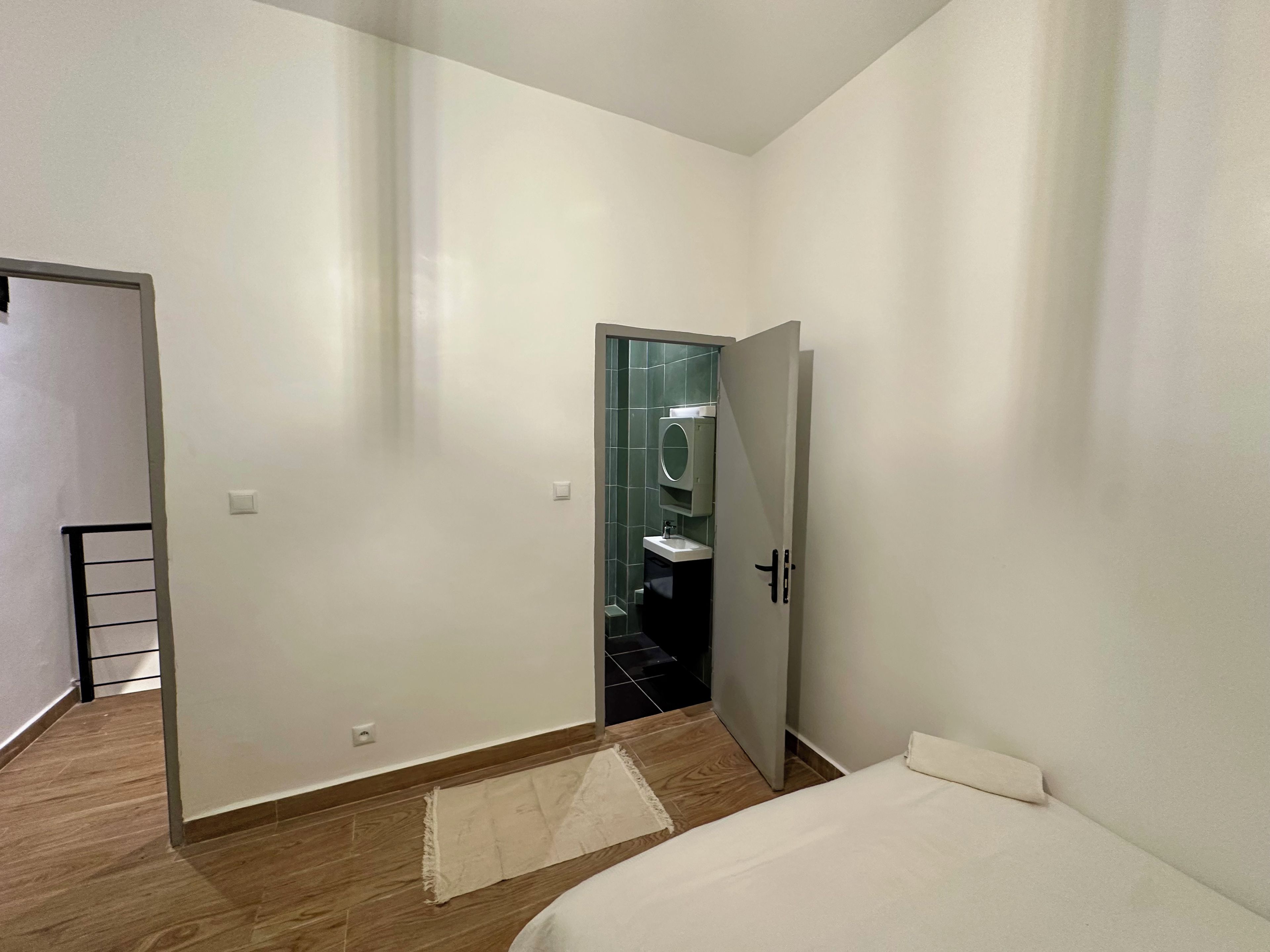 Un dormitorio con una cama, una puerta que da al baño y una alfombra pequeña en el suelo.