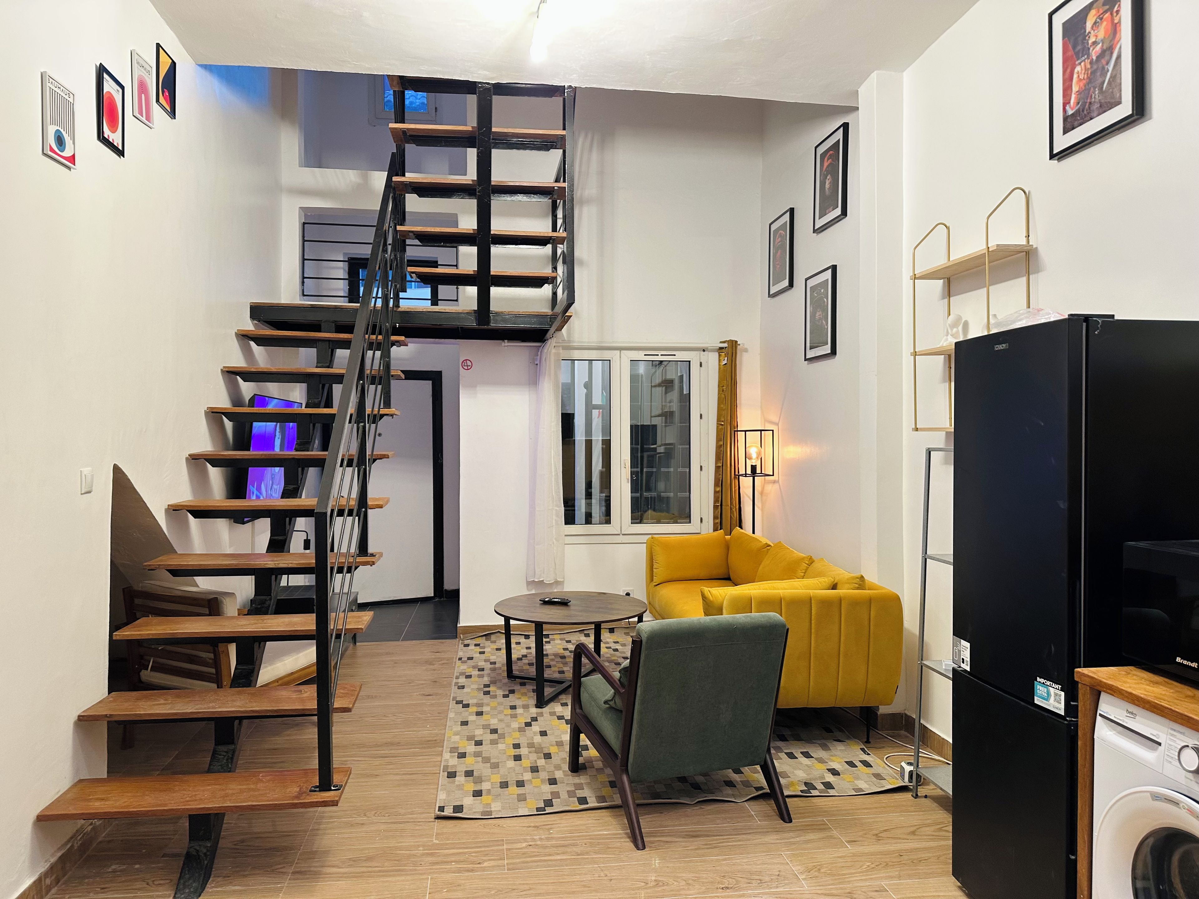 Un espacio habitable compacto con escalera, sofá, lavadora y mesa de comedor.