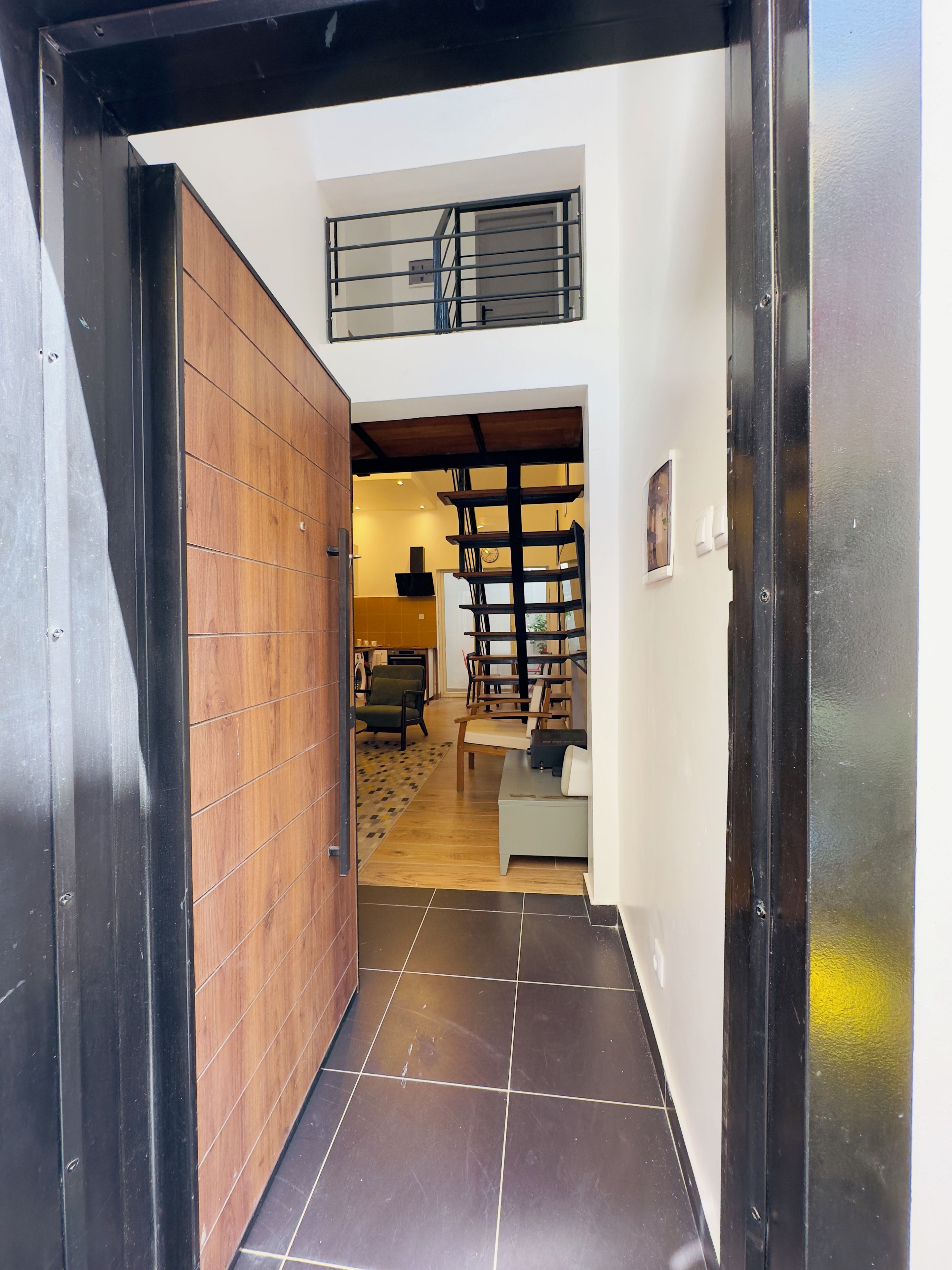 A hallway with a wooden door, a tiled floor, and a staircase leading to an upper level.