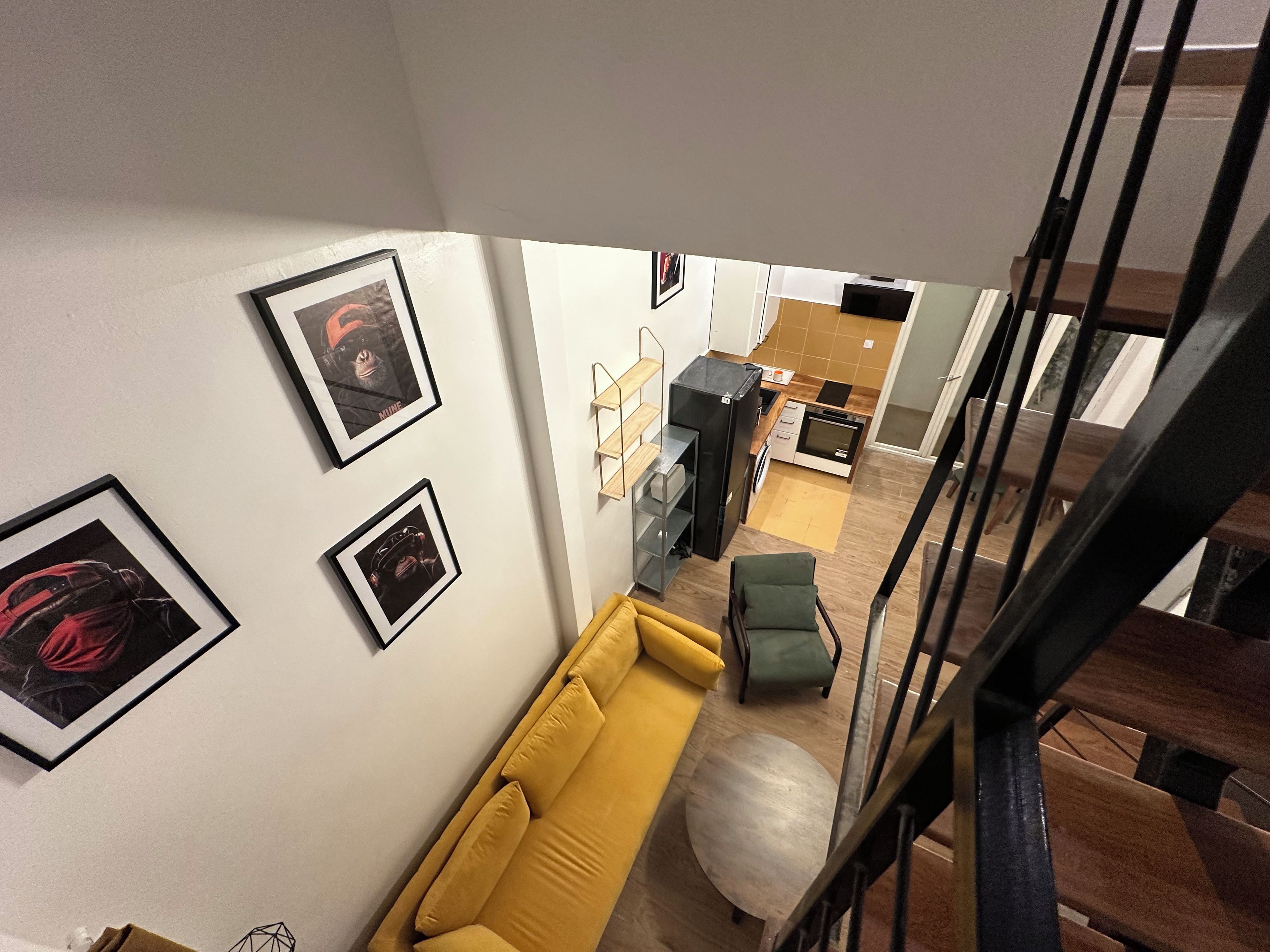 Ein modernes Interieur mit einem gelben Sofa, einem runden Hocker und gerahmten Kunstwerken an den Wänden.