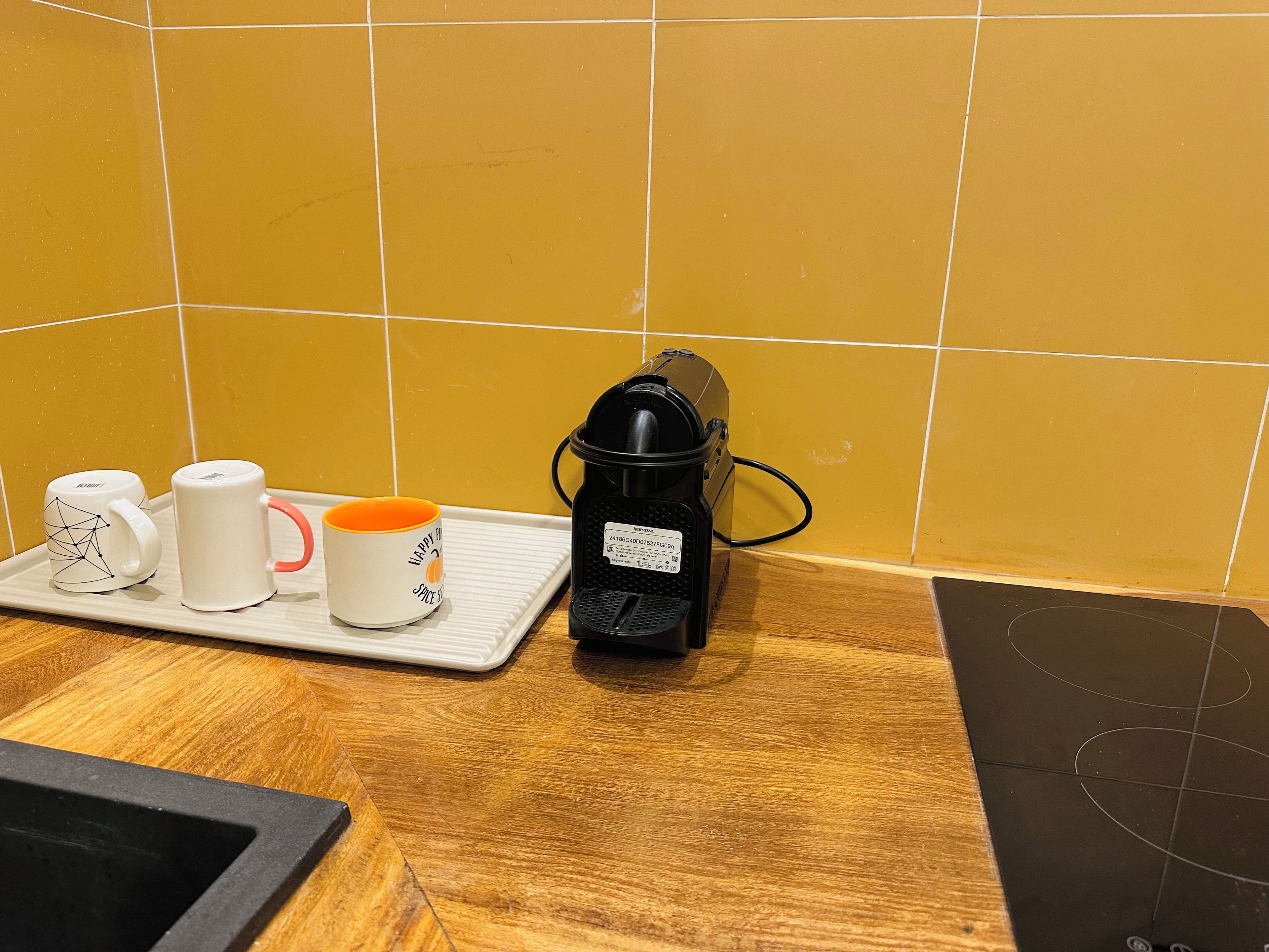 Eine Küchenarbeitsplatte mit einer Kaffeemaschine, einer Schale mit zwei Tassen und einer gefliesten Spritzschutzwand.