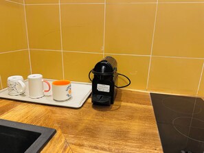 Eine Küchenarbeitsplatte mit einer Kaffeemaschine, einer Schale mit zwei Tassen und einer gefliesten Spritzschutzwand.