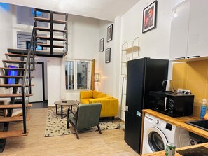A compact living space with a staircase, a sofa, a washing machine, and a microwave. - Urban Loft Dakar: "Patte d'Oie"—Air Conditioning and Comfort (Dakar)