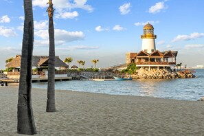 Um edifício costeiro com um farol, uma praia e palmeiras.