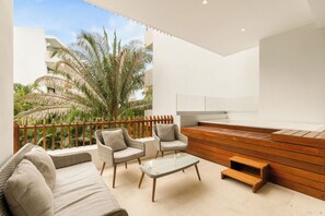 Uma área externa moderna com um banco de madeira, duas cadeiras de vime e um sofá.