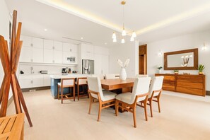 A modern kitchen with white cabinets, a central island, and a dining area with wooden chairs and a table. - Jungle Oasis 2BR | Luxury Beach Club + 5 Pools (Cruz de Huanacaxtle)