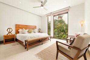 A bedroom with a wooden bed, a nightstand, a chair, and a large window with a view of greenery. - Jungle Oasis 2BR | Luxury Beach Club + 5 Pools (Cruz de Huanacaxtle)