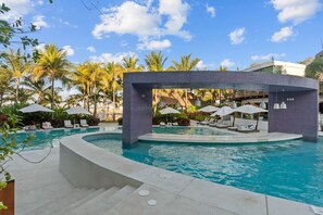 A swimming pool with a tiled structure, lounge chairs, umbrellas, and palm trees. - Jungle Oasis 2BR | Luxury Beach Club + 5 Pools (Cruz de Huanacaxtle)