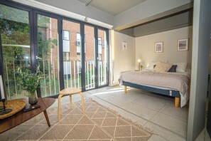 A bedroom with a bed, a desk, a chair, and a view of a building through a glass door. - Study with a large window · Featured design (H07) (Providencia)