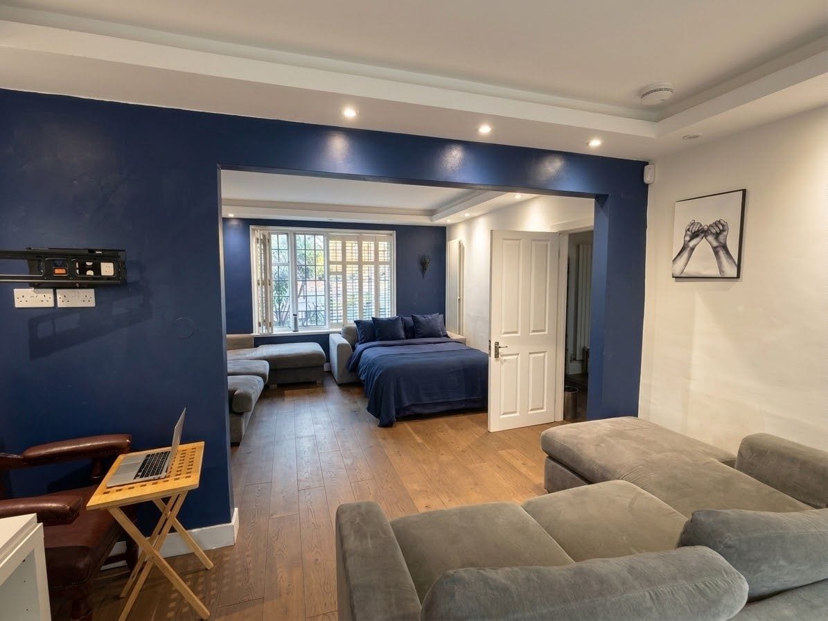 Une pièce comprenant un lit, un bureau et une chaise. Il y a une fenêtre avec des stores, une porte et une étagère fixée au mur.